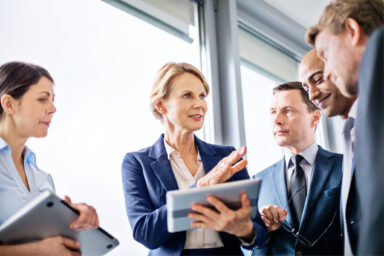 2 Frauen und 3 Männer im Anzug stehen zusammen und unterhalten sich.