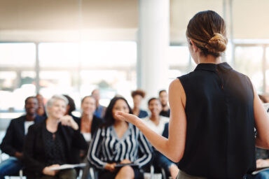 Eine Frau steht vor Publikum und redet.