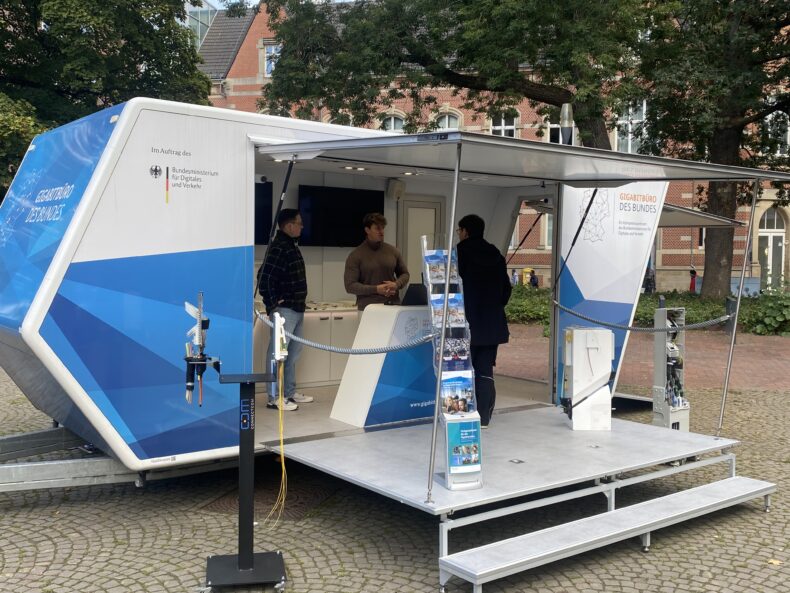Auf dem Bild ist das Gigabit-Mobil des Gigabitbüro des Bundes zu sehen. Es zeigt unsere Expertinnen und Experten im Gespräch mit einem Bürger.