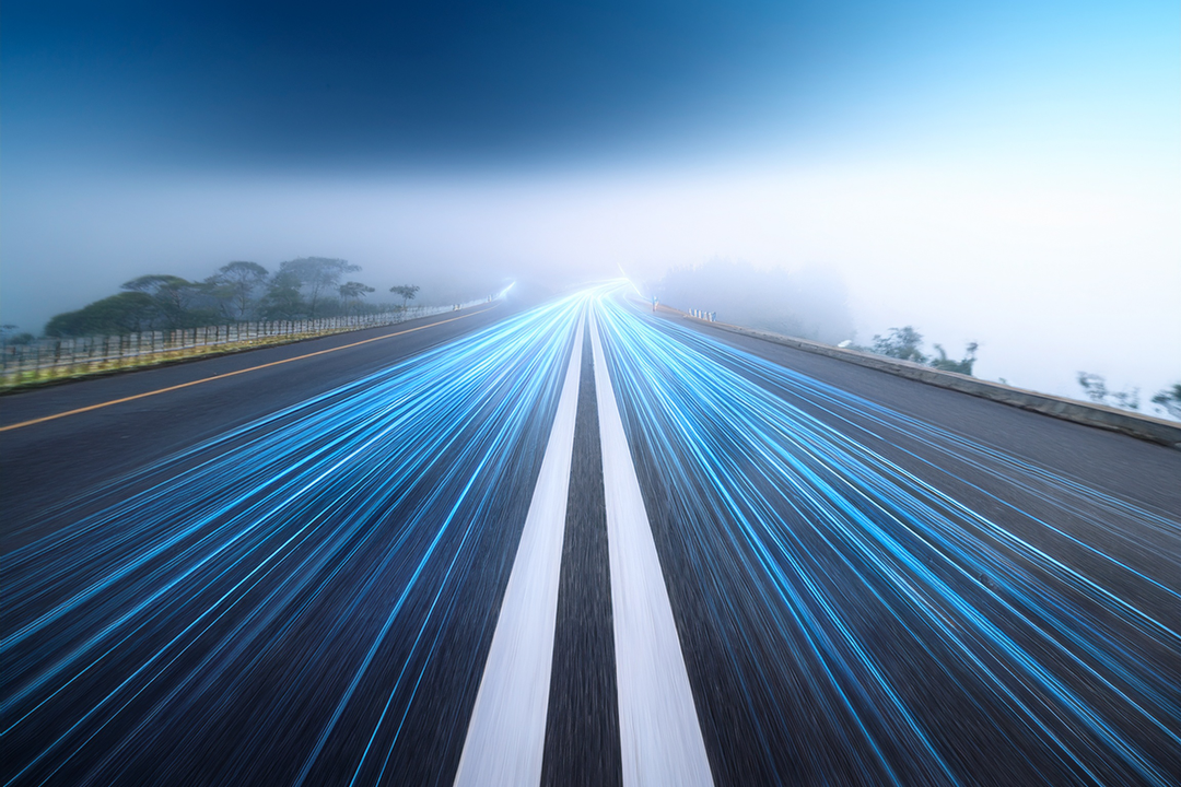 Zwei Autobahnspuren, die von Glasfasern geführt werden. Hinten eine vernebelte Landschaft.