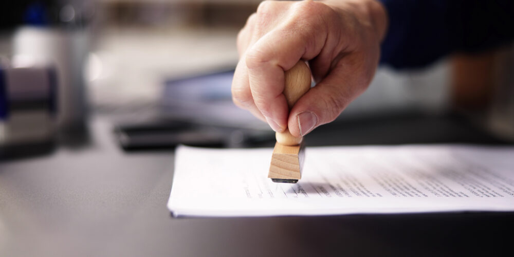 Auf dem Foto setzt jemand ein Stempel auf ein Dokument.