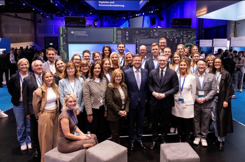 Großes Gruppenfoto von rund 40 Personen auf dem Messestand des Bundesministeriums für Digitales und Staatsmodernisierung.